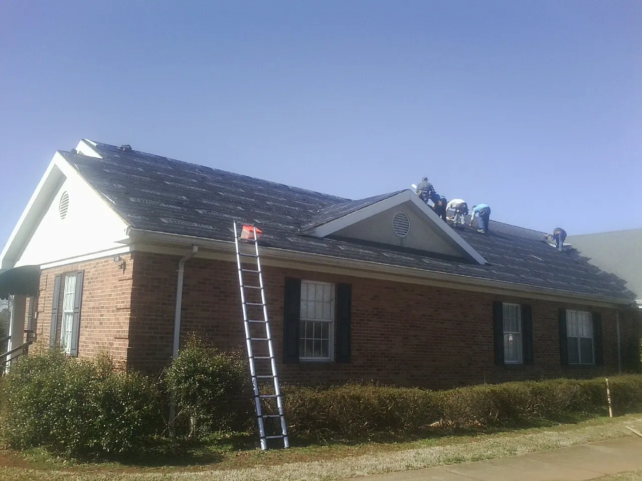 Crew tearing shingles off a brick ranch roof with a ladder set — Metal Roof Repair work by our crew in Englewood Cliffs