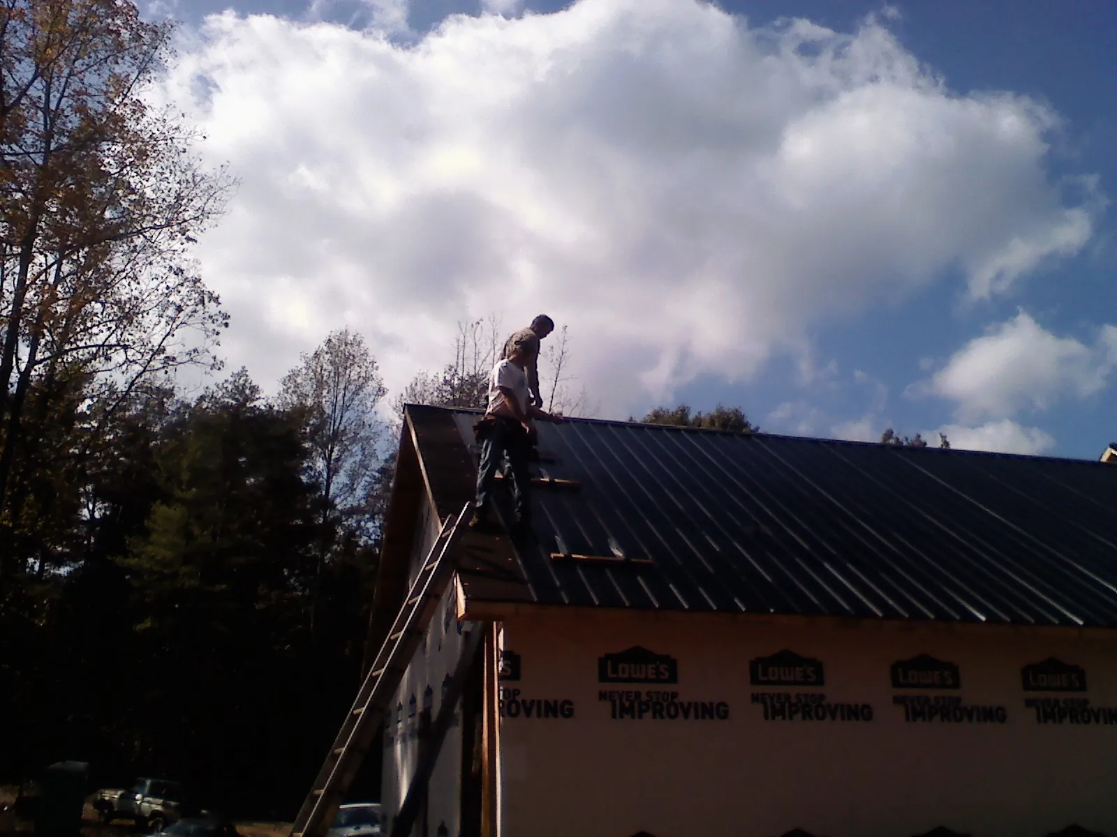 Roofer fastening dark metal panels high against a cloudy sky, from a Roof Inspection job in Englewood Cliffs