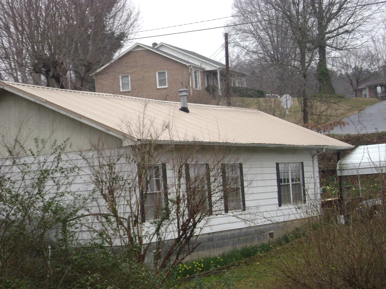 Tan metal roof on a white sided house set into a hillside — Commercial Roofing by Roofing Brothers in Englewood Cliffs